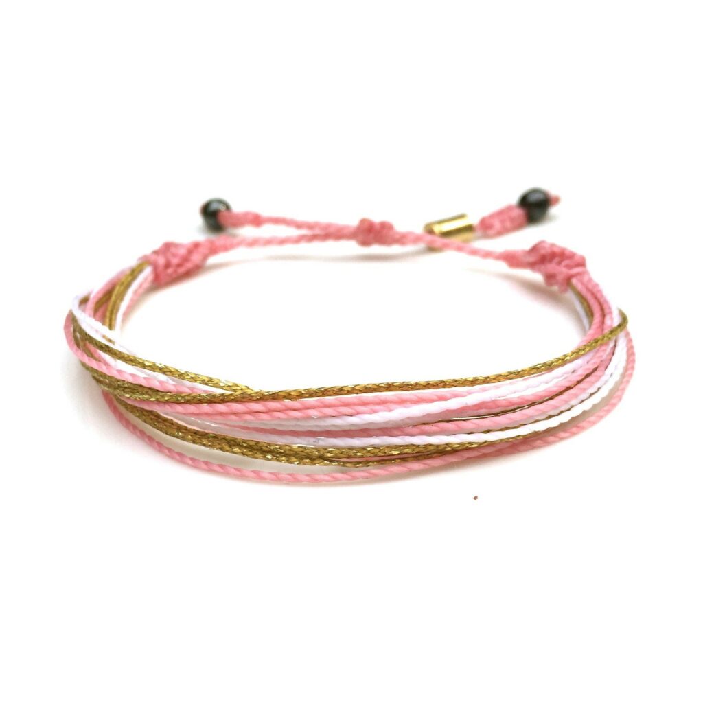 Pink string bracelet with metallic gold and white accents size adjustable with pull tie for men, women and kids. Rumi Sumaq surfer string bracelets are handmade on Martha's Vineyard by designer Coco Paniora Salinas.